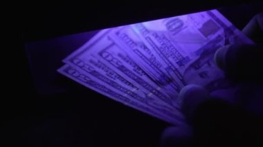 Ultraviyole ışık altında dolar banknotuna odaklanın. Benjamin Franklin 'in portresi incelendi. Sahte para konseptinin arka planı. Ultraviyole lambanın altında dolarları kontrol ediyorum. bir tomar para