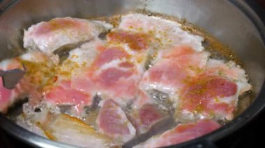 Yakından, kızgın yağda pişmiş et ve dökme demir tava. Kızarmış pastırma dilimleri. Kızartma tavasında leziz domuz eti. Kadının eli çatalla kavrulmuş parçaları ters çeviriyor..