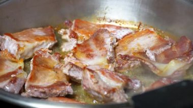 Yakından, kızgın yağda kavrulmuş et, dökme demir tavada kızartılıyor. Kızarmış pastırma dilimleri. Kızartma tavasında sulu et. Kızarmış biftek pişirme işlemi.