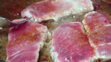 Yakından, kızgın yağda pişmiş et ve dökme demir tava. Kızarmış pastırma dilimleri. Kızartma tavasında leziz domuz eti. Kadının eli çatalla kavrulmuş parçaları ters çeviriyor..