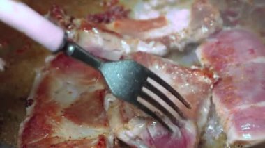 Yakından, kızgın yağda pişmiş et ve dökme demir tava. Kızarmış pastırma dilimleri. Kızartma tavasında leziz domuz eti. Kadının eli çatalla kavrulmuş parçaları ters çeviriyor..