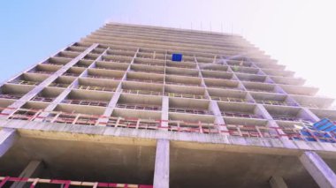 Mavi gökyüzüne karşı büyük ve uzun tamamlanmamış bir ev. Alt manzara, kamera dönüyor ve binaların resimlerini çekiyor sağdan sola, dönerek. İnşaat alanı, müteahhit. Apartman kompleksi biçiminde nesne teslimatı.