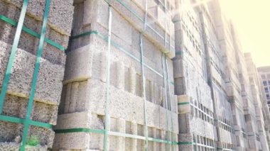 Büyük bir yığın sünger taşı ve bloklar paletler halinde küp şeklinde paketlenmiş. İnşaat alanı, kamera hareketi, inşaat ve güneş ışığının arka planına karşı çok sayıda blok.