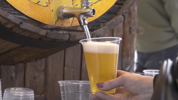 祭りやお祝い 女性の手のクローズアップは 蛇口からプラスチックの使い捨てカップに木製の樽からビールを注ぎます アルコールフェア ビールを飲むと酔う — ストック動画