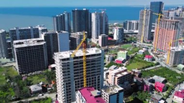Yaz günü yüksek binaların deniz ve dağların zeminine bakan insansız hava aracı manzarası. Gürcistan 'da Batumi deniz kıyısında yoğun inşaat malzemeleri ve inşaat malzemeleri var..