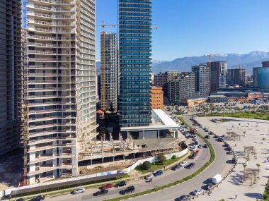 Batumi, Georgia - 28 Mart 2023: İnşaat halindeki çok katlı binaların insansız hava aracı görüntüsü, oteller, modern binalar, güneşli bir günde dağların arka planına karşı yeni bir bulvarda bir yol.