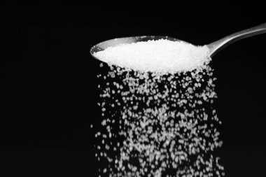 Siyah zemin üzerinde ufalanan beyaz şekerli çay kaşığının makro fotoğrafçılığı, boşluğu kopyala.