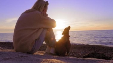 Genç ve güzel bir kadın deniz kenarında kayalarda oturuyor ve köpek yavrusu teriyeriyle birlikte ufuk çizgisinde gün batımını seyrediyor. Hayvanlar için dostluk ve sevgi. Çocuklardan özgürlük.