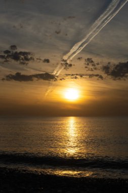 Bulutlar ve dikey bir uçağın izi ile denizde güzel sihirli bir günbatımı. Güneş ufukta batarken inanılmaz yumuşak bir gün batımı.