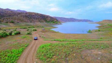 Ermenistan 'a yolculukta kırsal yollar ve dağlar arasında göl boyunca giden aracın insansız hava aracı görüntüleri. Doğal manzara Azat rezervuarı. Wilderness Filmi. Arabayla seyahat etmek.
