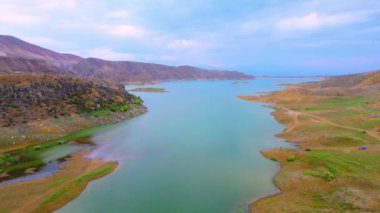 Dağ gölündeki hava manzarası. Dağ vadisindeki su deposunda insansız hava aracı. Dağlık araziler arasında dağ gölünün pürüzsüz mavi yüzeyinden güzel bir manzara. Azat