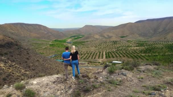 ドローンの飛行アルメニアの谷で美しい高い山や田舎の開口部を見て観光客のカップルの横に飛んでいます 男と女は徒歩で旅行 — ストック動画