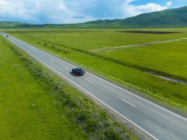 Siyah yolcu vagonu, güneşli bir günde yeşil tarlalar boyunca asfalt bir yolda ilerliyor. İnsansız hava aracından fotoğraf çekmek. Seyahat kavramı