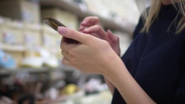 Güzel genç bir kadının portresi mağazadan yeni ayakkabılar alıyor, telefon uygulamasına bakıyor ve indirim ya da fiyat arıyor. Halk alışverişi kavramı. Güzel kız ayakkabılarını seçer.