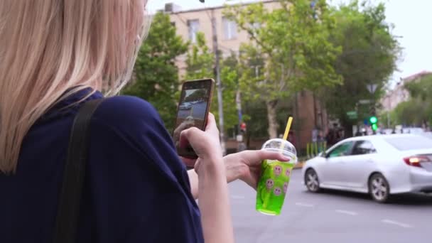 年轻女性博主在城市街道和城市的背景下 用装有吸管的玻璃杯鸡尾酒手机相机拍照 分享照片和视频在社交媒体上 著名博客 — 图库视频影像