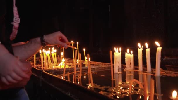 キリスト教正教会の人々の手のライトキャンドル 寺院の暗い神聖な内部でのろうそくの炎 記念のろうそくは教会で点灯されます 戦争や悲しみの象徴 出来事の記憶 — ストック動画