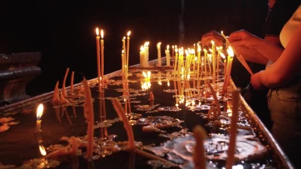 人们的手在基督教正教会点燃蜡烛 在圣殿黑暗的神圣内部点燃着蜡烛 教堂里点燃着纪念蜡烛 战争或悲伤的象征 对事件的记忆 — 图库视频影像
