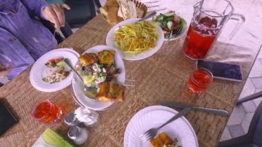Restoranda kızarmış balık yiyen ve sohbet eden mutlu bir kadın, kamerada konuşuyor. Masada kırmızı odun kompostosu, patates ve salata var. Akşam yemeği ve ucuz masa. Restoran Ucuz.
