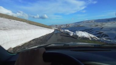 Arabadan içeriden birinci şahıstan, karlı dağlarda yol manzarası. Şoförün elleri direksiyonda, kışın araba sürüyor. Ermenistan, Aragats Dağı. Şoförün eli direksiyonda. Seyahat
