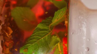 Çay demleme süreci, çay töreni, taze demlenmiş meyve ve bitki çayı. Bir kaşık çay demliğinde çay, çay yaprakları, nane, çilek ve cam çaydanlıkta meyve karıştırır. yakın plan.