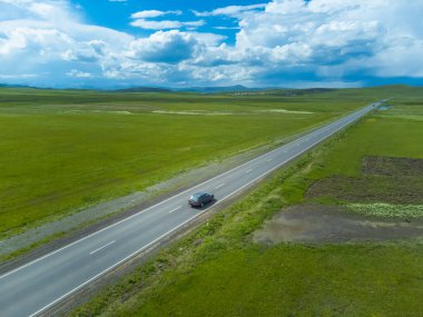 Gri yolcu vagonu yeşil tarlalar boyunca asfalt bir yolda, güneşli bir günde dağlar, gökyüzünde güzel bulutlar. İnsansız hava aracından fotoğraf çekmek. Seyahat kavramı