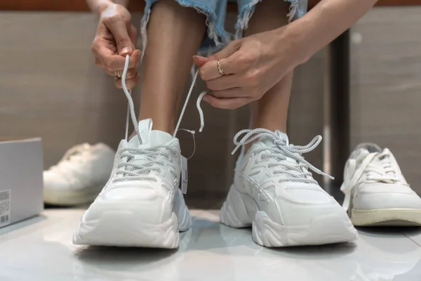 Zbliżenie Kobiet Nogi Wybierając Buty Sportowe Przymierzając Różne Białe Tenisówki — Zdjęcie stockowe