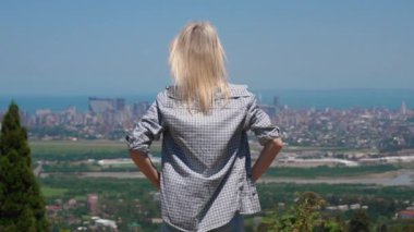 Kadın şehir manzarasını seviyor. Şehir ve denizin güzel paylarını küçümseyen genç bir kadın. O, yükseklikte gün doğumunu sever ve şehre tepeden bakar. Güneşli sıcak bir gün.