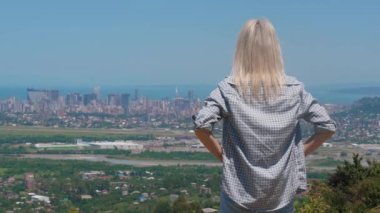Kadın şehir manzarasını seviyor. Şehir ve denizin güzel paylarını küçümseyen genç bir kadın. O, yükseklikte gün doğumunu sever ve şehre tepeden bakar. Güneşli sıcak bir gün.