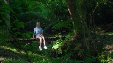 Nehir kenarındaki köprüde üzgün üzgün bir kız. Genç, güzel, beyaz bir kadın ahşap bir köprüde oturuyor ve etrafa bakıyor. Muhteşem bir manzara ve güzel bir orman Güneş ışığıyla muhteşem bir doğa.