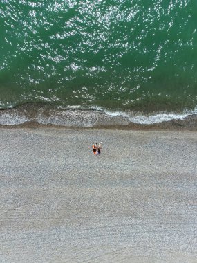 Bir erkek ve bir kadın, güneşli bir günde Karadeniz kıyısındaki çakıl taşlı bir plajda, bir dronun manzarasında uzanıyorlar. Dikey fotoğraf