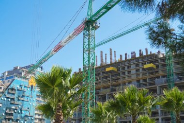Binaların, palmiye ağaçlarının, mavi gökyüzünün arka planına karşı bir inşaat vincinin yakın çekimi. Güzel inşaat alanı