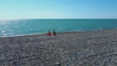 Çakıl taşlı plajdaki birkaç insanın hava görüntüsü. Boş Macera. Drone deniz dalgaları vuracak ve balaylarında aşık çiftlerin etrafında uçacak. Meet or Lovers. Okyanusta rahatla. Yeşil deniz ve taşlar.