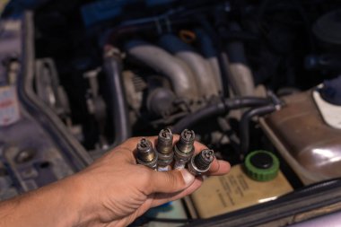 Motorun arka planında dört kullanılmış araba mumu olan bir elin yakın çekimi. Araba tamiri kavramı