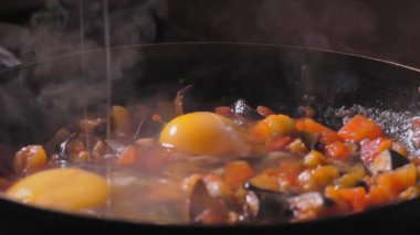 Tavada sebzeli yumurta kasesi. Ev yapımı Shakshuka. Şef kızarmış sebzelere kırık yumurta ekler. Yavaş çekim, taze sebzelerden yapılan vejetaryen yiyecekler..