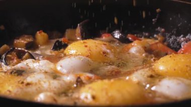 Tavada sebzeli yumurta. Ev yapımı Shakshuka. Şef yumurta sarısına baharat ve kırmızı biber ekler. Yavaş çekim, taze sebze ve yumurtadan yapılan vejetaryen yiyecekler..