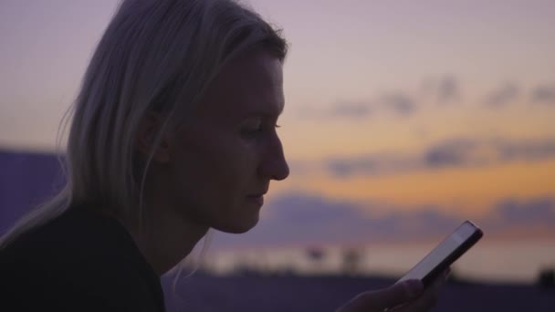 在日落 假期和夏天的时候 年轻的女游客在海滩上带着手机 通信在信使 网络空间和网络业务 女商人 远程工作 — 图库视频影像