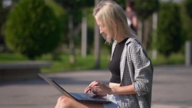 Serbest çalışan kadın ya da iş kadını parkta bankta otururken dizüstü bilgisayar kullanır. İnternette çalışan ya da bilgisayarla çalışıp öğrenen genç bir kadın. Güneşli yaz günü.