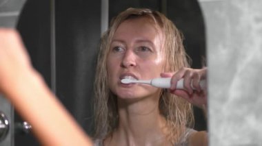 Beyaz dişlerini modern elektrikli diş fırçasıyla fırçalayan genç bir kadının portresi. Yakın plan. Diş hekimliği, günlük bakım, ağız temizliği ve diş temizliği. Sağlık hizmetlerinde sabah işlemleri,