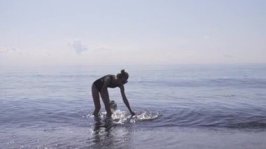 Genç bir kadın, çöpleri ve plastik torbaları çubukla denizden topluyor. Deniz ya da okyanus kirliliği. Çevresel koruma. Plastik enkazı denizden toplamak ve geri dönüşüme göndermek için. Genel atık sorunu.
