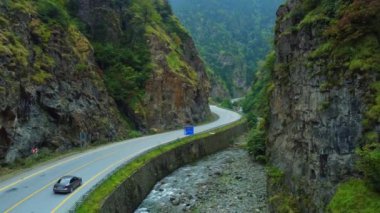 Dağ nehri boyunca ormandaki dağ yolunun havadan görünüşü. Güzel manzara. Çarpıcı dağlık bölgeler. Asfalt yolunun yaz manzarası. İnanılmaz doğal bir manzara. Vahşi Yaşam Filmi