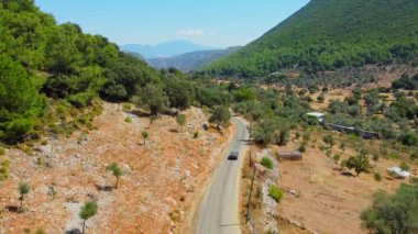 İnsansız hava aracı, Türkiye 'de binalar, evler ve ağaçlarla dolu dağ geçitlerine doğru giden kırsal yol boyunca giden otomobili izliyor. Dağların eteğindeki tarım arazisi. Sıcak güneşli bir gün, romantizm. Tatilde araba gezisi..