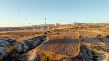 Nevsehir, Goreme, Kapadokya 'daki peri bacaları vadisinde uçan renkli sıcak hava balonları. Yeraltı şehri ve sıcak hava balonu turizminin nefes kesici panoramik drone görüntüsü.
