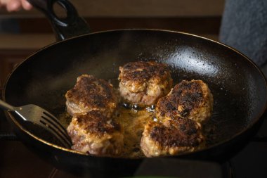Kızartma tavasında kıymalı pirzola yakın plan. Aşçı tavadaki pirzolaları çatalla çeviriyor. Pirzolaların Rusça veya Lehçe versiyonu - kotlety.