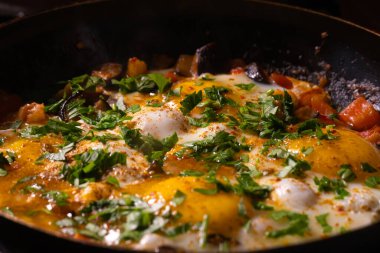 Kızarmış tavuk yumurtaları, domatesler, baharatlı patlıcan ve kızartma tavasında taze maydanoz. Yemek pişirme süreci, seçici odaklanma. Kahvaltı için ev yemeği.