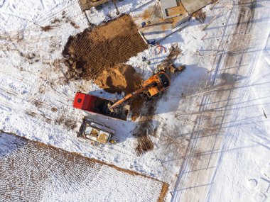 Kazıcının bir kamyona kum döken hava görüntüsü. İnşaat alanının kışın en üst manzarası. Bir İHA 'dan ateş etmek.