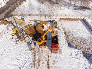 Kazıcının bir kamyona kum döken hava görüntüsü. İnşaat alanının kışın en üst manzarası. Bir İHA 'dan ateş etmek.