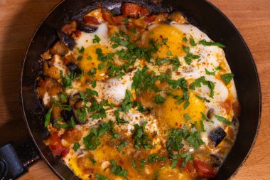 Kızarmış tavuk yumurtaları, domatesler, baharatlı patlıcan ve kızartma tavasında taze maydanoz. Yemek pişirme süreci, seçici odaklanma. Kahvaltı için ev yemeği.