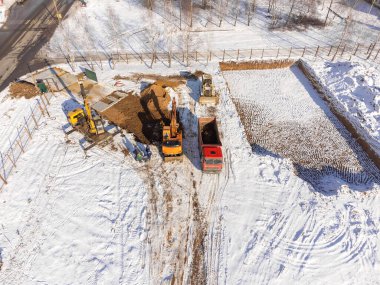 Kazıcının bir kamyona kum döken hava görüntüsü. İnşaat alanının kışın en üst manzarası. Bir İHA 'dan ateş etmek.