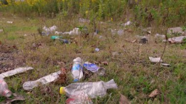 Ormana çöp yığını, doğaya rastgele çöplük. Pis kokulu yığın, plastik torba ve şişeler, doğanın kirli yeşil çimenlerindeki çöpler. Orman kirliliği kavramı. Yiyecek konteynırları parkın etrafına saçılmış.,