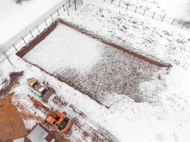 İnşaat alanının kışın başındaki insansız hava aracı görüntüsü. Kazıcı, buldozer kış mevsiminde inşaat alanında.